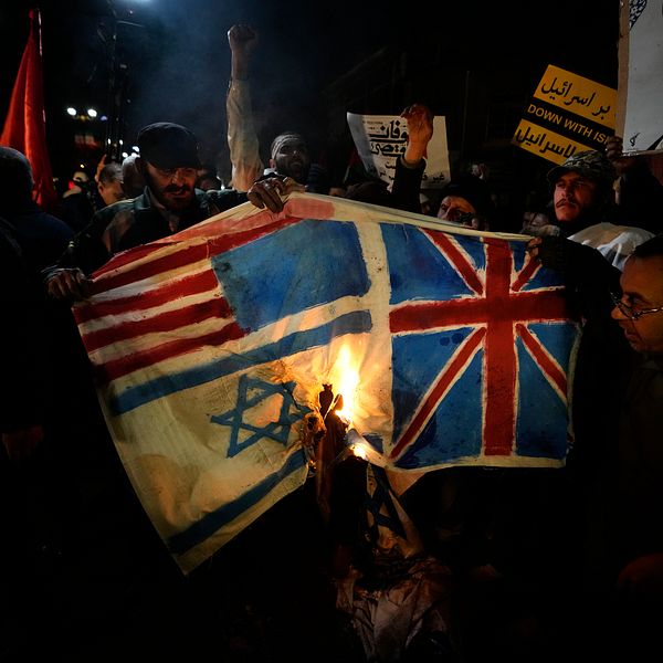 En grupp män sätter eld på en bit tyg eller papper som föreställer USA:s, Israels och Storbritanniens flaggor.