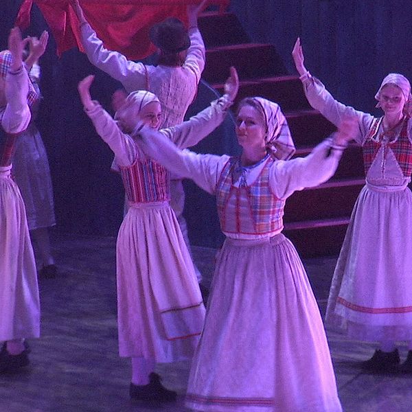 Kvinnor i folkdräkt dansar på scen under en teaterföreställning.
