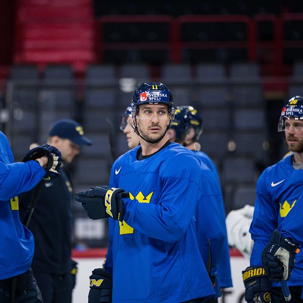 Ishockeyspelare i blå tröjor samtalar under ett träningspass i ishall.
