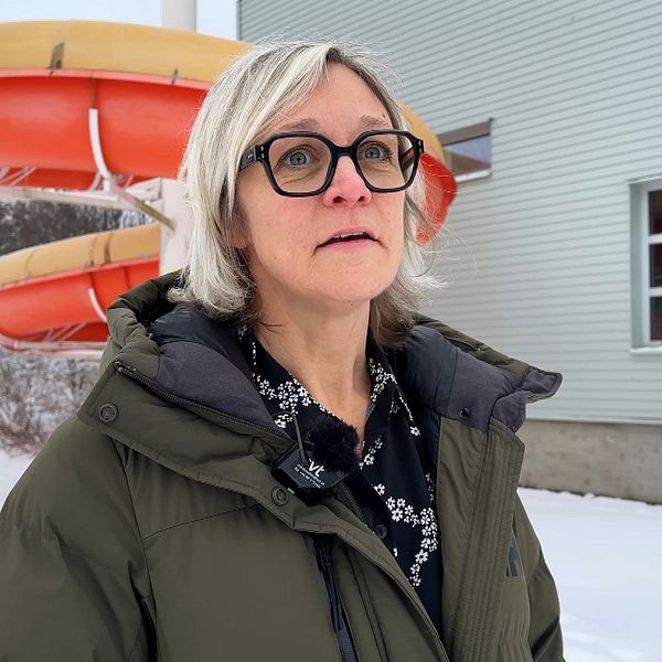 Åsa Säfsten Boman, verksamhetschef för bad i Umeå, i en mörk vinterjacka står utanför badhuset Storsjöhallen i Holmsund. Badhuset med röda rutschkanor i bakgrunden, omgiven av snötäckta omgivningar.