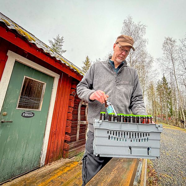 Man står vid en röd byggnad och håller en låda ölflaskor.