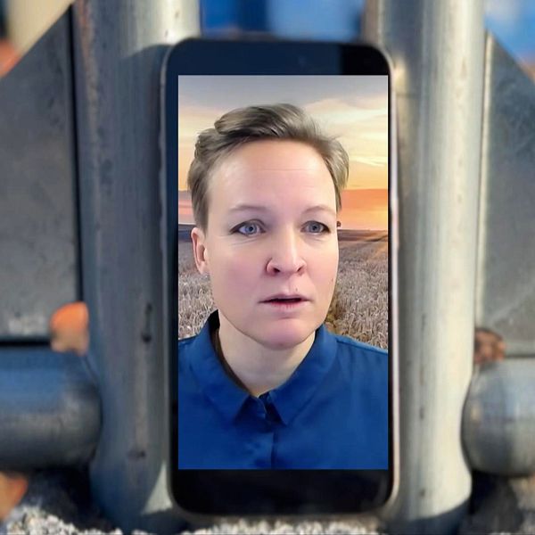 En mobiltelefon är placerad mellan två metallstänger med en bakgrund som visar en landskapsvy vid solnedgång. Mobilskärmen visar en person i blåt tröja, omgiven av en oskarp, urban miljö. Bilderna och omgivningen ger en känsla av modern kommunikation i en industriell setting.