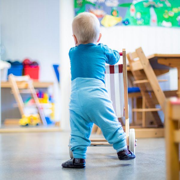 Ett litet barn som går bakom en leksaksvagn i en ljus och färgglad förskolemiljö.
