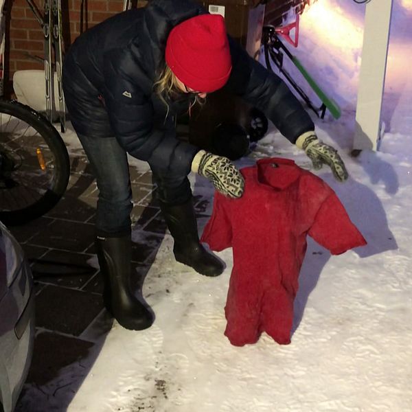 en kvinna i dunjacka och mössa ställer en t-shirt som är stelfrusen, på den snöiga marken