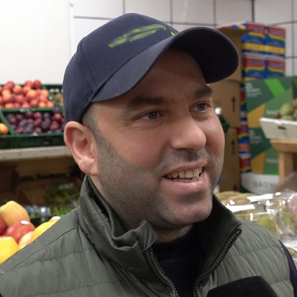 Person i butik med hyllor fyllda med frukt och grönsaker i bakgrunden.