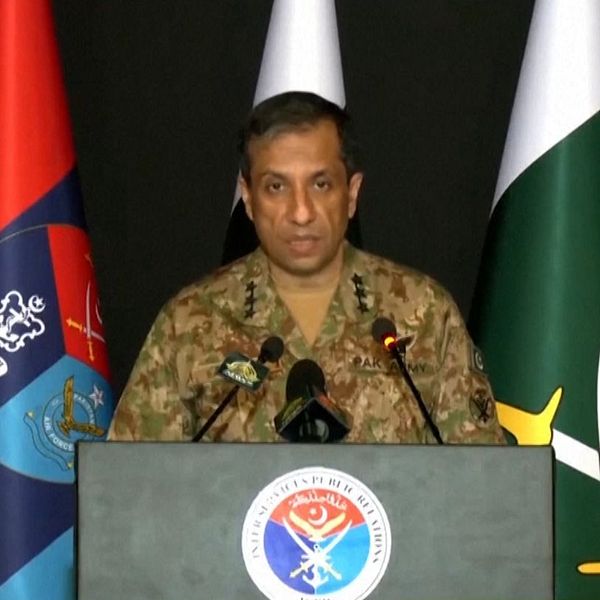 Pakistansk militärperson talar vid podium med flera flaggor i bakgrunden och urdu-text längst ner.