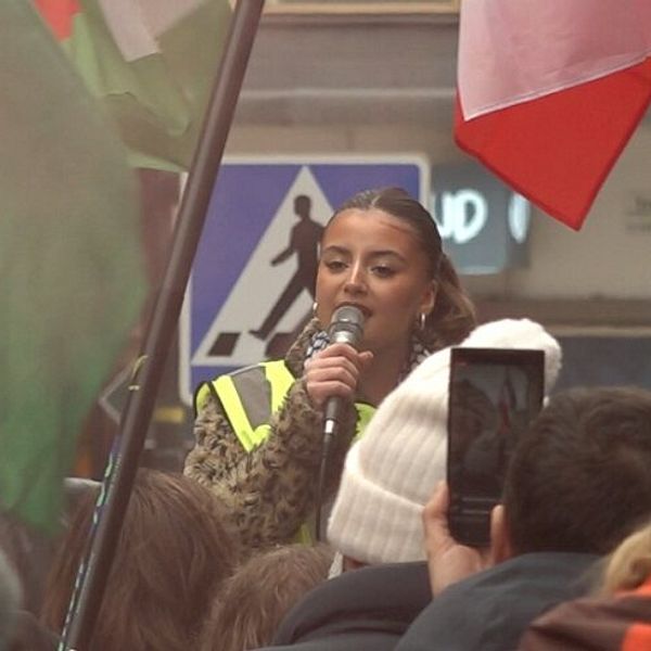 Ung kvinna talar i en mikrofon på en demonstration för elduppför i Gaza.