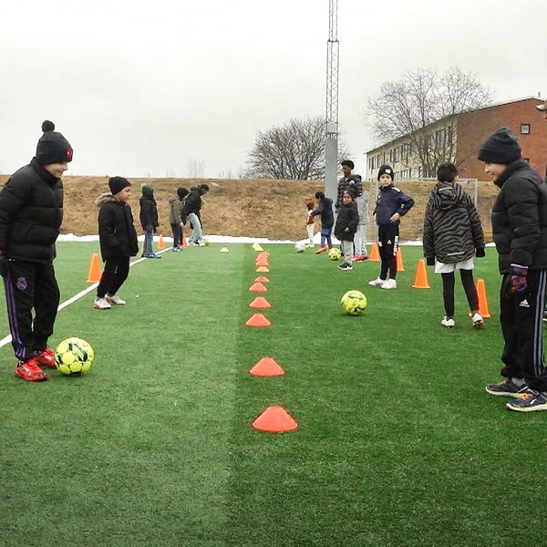 Barn på en fotbollsplan med koner och fotbollar.