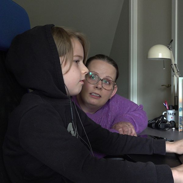 En pojke sitter vid en dator och hans mamma sitter bredvid