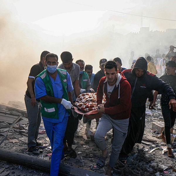 Människor i Gaza bär en person på en bår genom rasmassorna efter en attack.