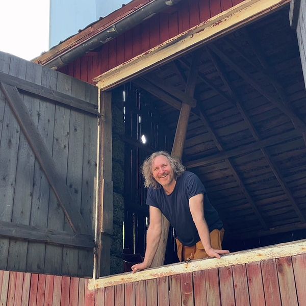 En man står och tittar ut från sin lada.