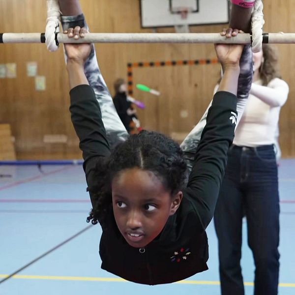Barn tränar gymnastik med handledares hjälp i en gymnastiksal.