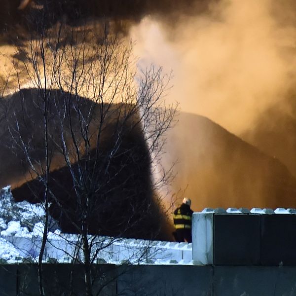 Brandman sprutar vatten på en stor svart hög med gummiflis