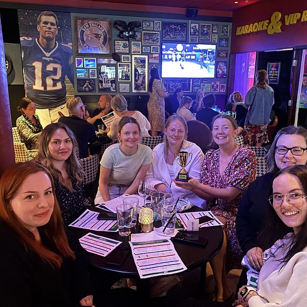 Flera personer sitter vid ett bord på en sportbar, en kvinna håller i en pokal.