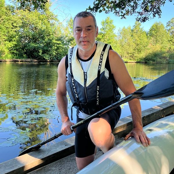 Man sitter vid upp och nedvänd kayak med paddel