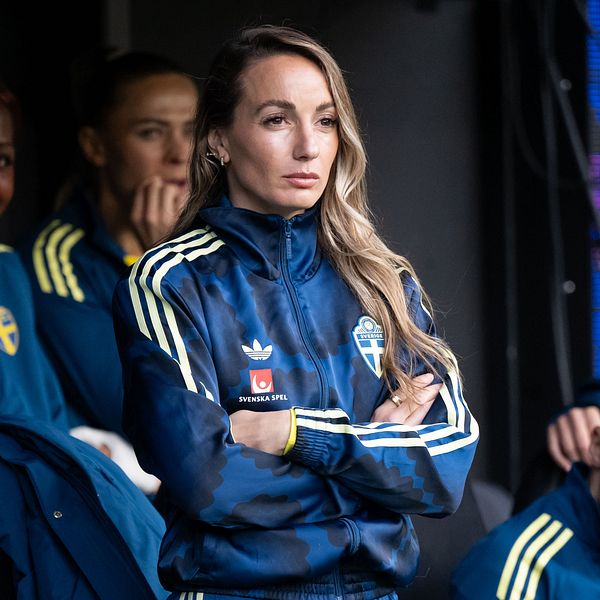Kosovare Asllani i blågul landslagsjacka på bänken med lagkamrater