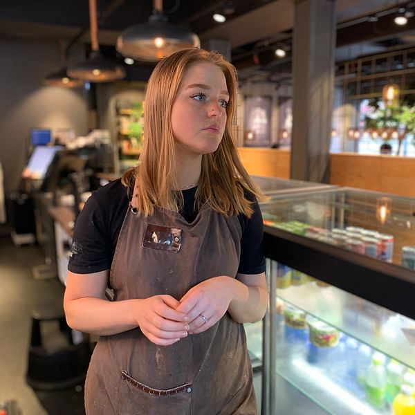 Ung kvinna står i en cafémiljö i Vetlanda. Ser sorgsen ut.
