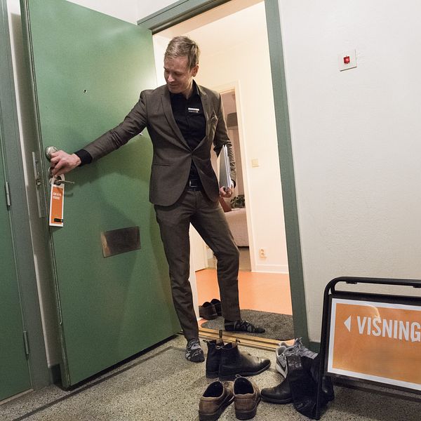 Man öppnar dörren till en bostadsvisning med skylt vid entrén