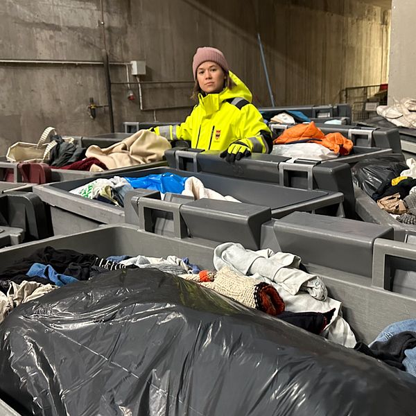 Karolina Werme på Örebro kommuns avfallshantering arbetar bland flera containrar fyllda med begagnade kläder och textilier i en industrimiljö.