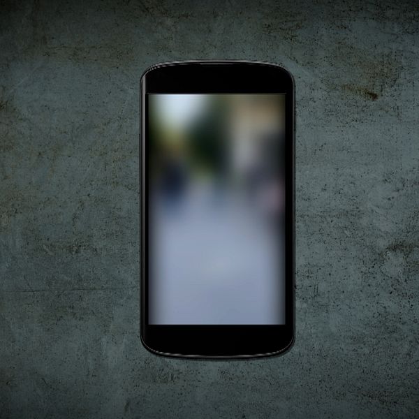 En mobil ligger på ett betonggolv, på skärmen visas en suddig video