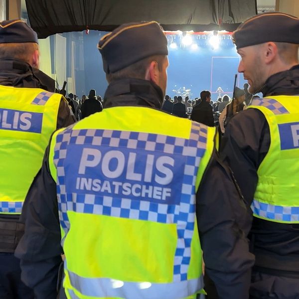 Tre poliser i reflexvästar övervakar en folksamling inomhus.
