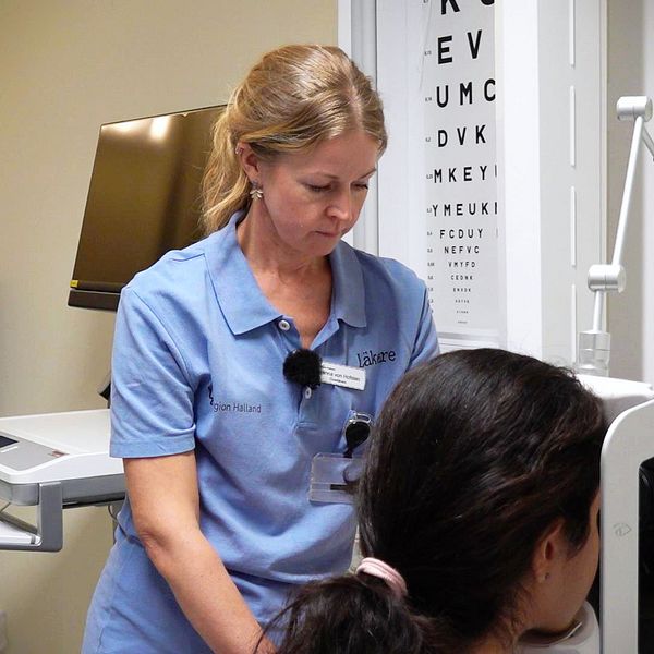 En läkare gör en ögonbottenundersökning. I bakgrunden syns en bokstavstavla.