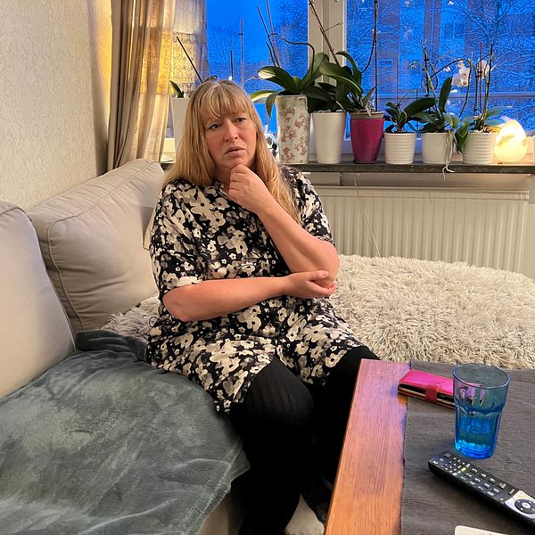 Kvinna sitter i en soffa framför ett fönster, har ena handen mot hakan.