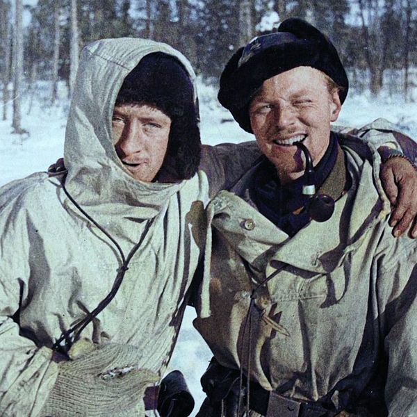 Två personer i vinterkläder står tillsammans i ett snöigt skogslandskap.