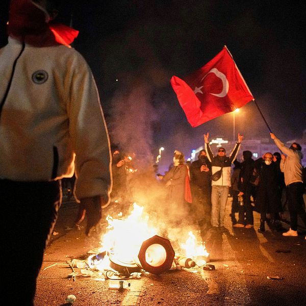 Folkmassa med turkiska flaggor kring eld, nattprotest.