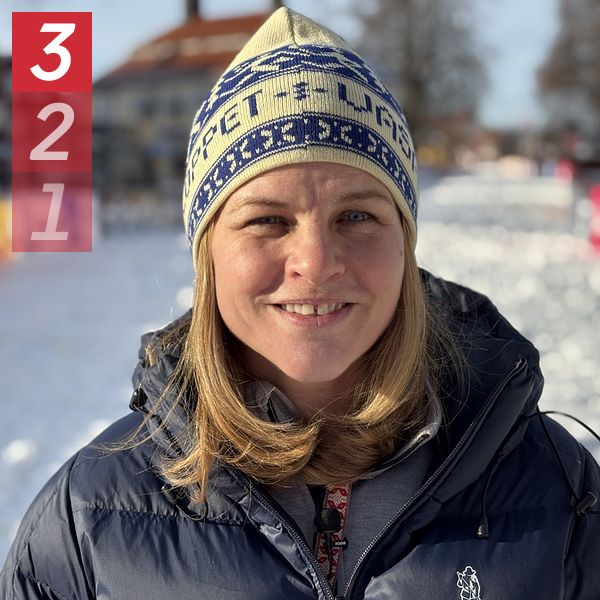 Person i vinterjacka och mössa står på en snöklädd gata med hus i bakgrunden.