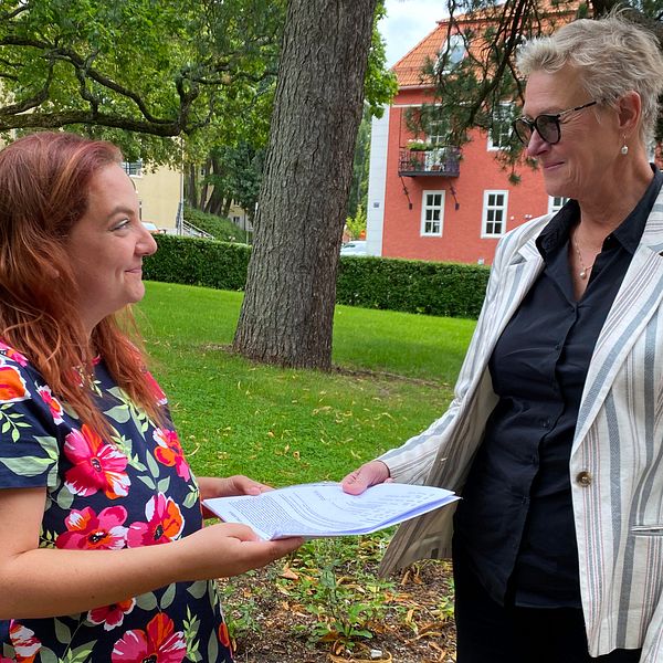 Anna Ekman-Brescia, en kvinna med blommig blus och rött hår, lämnar över en namnlista till förvaltningschefen för tandvård i Dalarna, en äldre kvinna med randig kavaj.