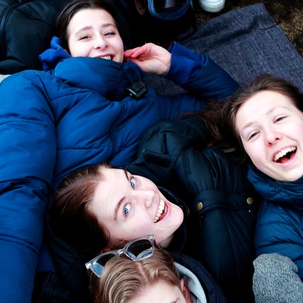 Tre unga tjejer ligger på marken i kön till Östgöta Nations valborgsbiljetter.