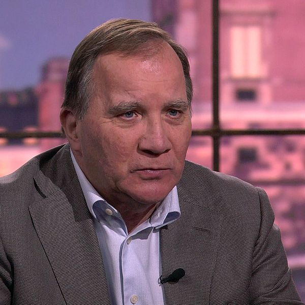 Stefan Löfven i grå kavaj intervjuas i tv-studio med stadsmiljö i bakgrunden.