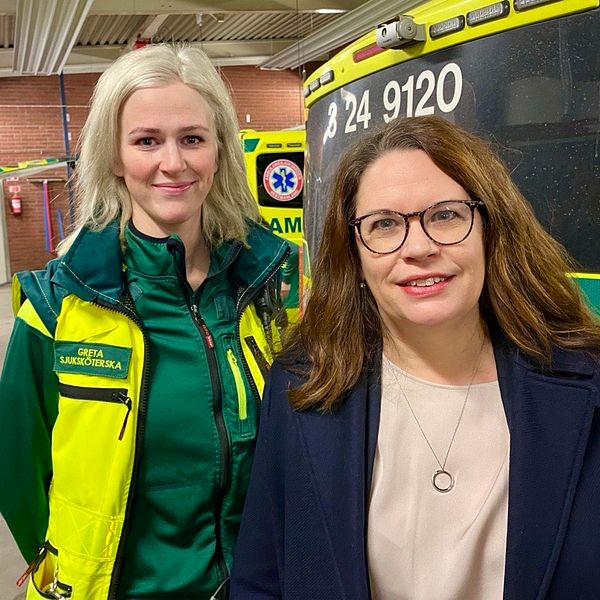 Ambulanssköterskan Greta Berglund står bredvid regionråd Malin Gabrielsson i ambulansgaraget.
