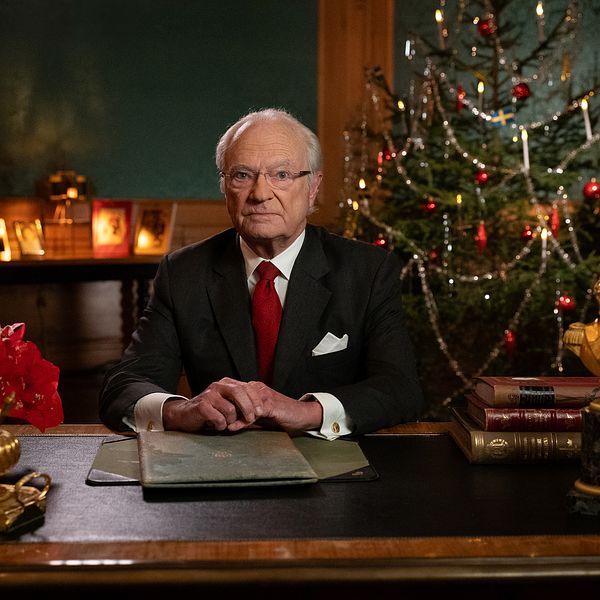 Hans Majestät Konungen sitter vid ett skrivbord omgiven av julpynt och en julgran i bakgrunden.