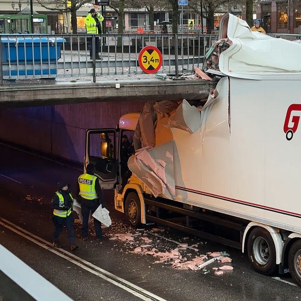 Lastbil från GTS Frakt har fastnat under en bro och fått sin trailer skadad, med delar av taket sönder. Två personer i reflexvästar inspekterar skadan och försöker lösa situationen. En skylt på bron visar höjdbegränsningen på 3,4 meter.