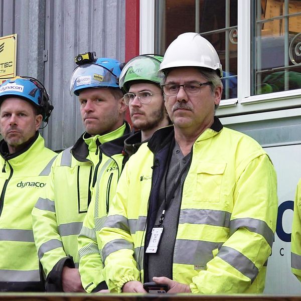 Sex byggarbetare står med sammanbitna miner under den tysta minuten.
