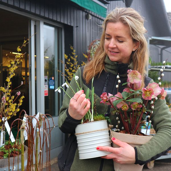 Kvinna vid trädgårdshandel håller i en krukväxt och ett blommande arrangemang.