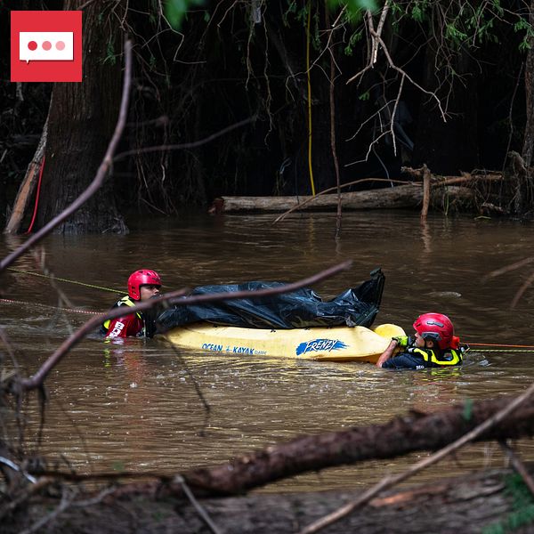 Räddningsarbetare i vatten under översvämning, omgivna av träd och brunt vatten.