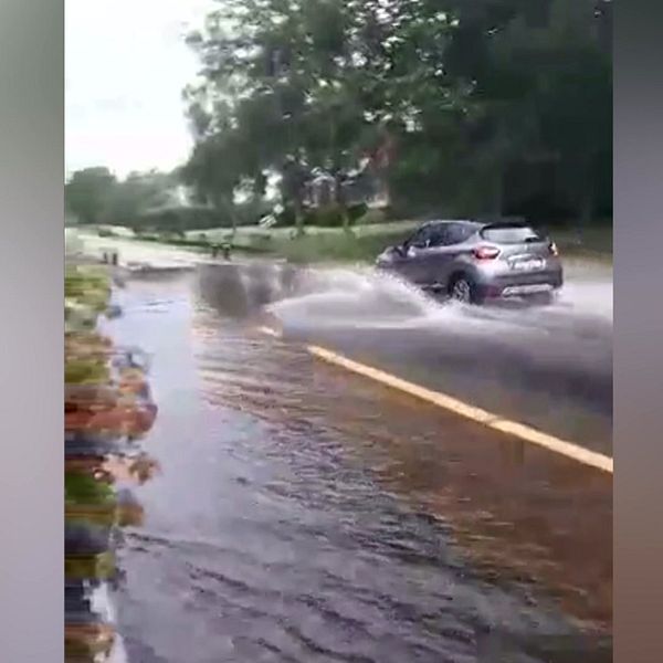 Bil kör in i en översvämmad väg.