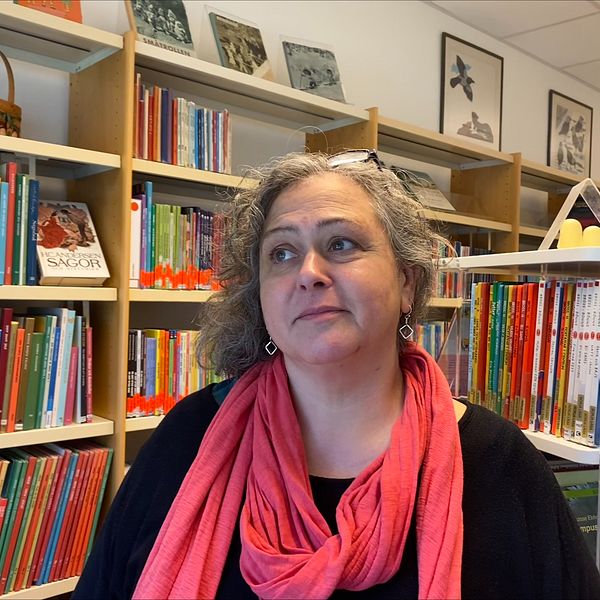 Lotta Lejon Stenberg står framför bokhylla på bibliotek.