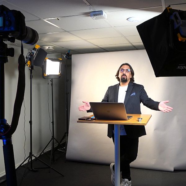 En person håller digital föreläsning framför kamera och strålkastare i studio.