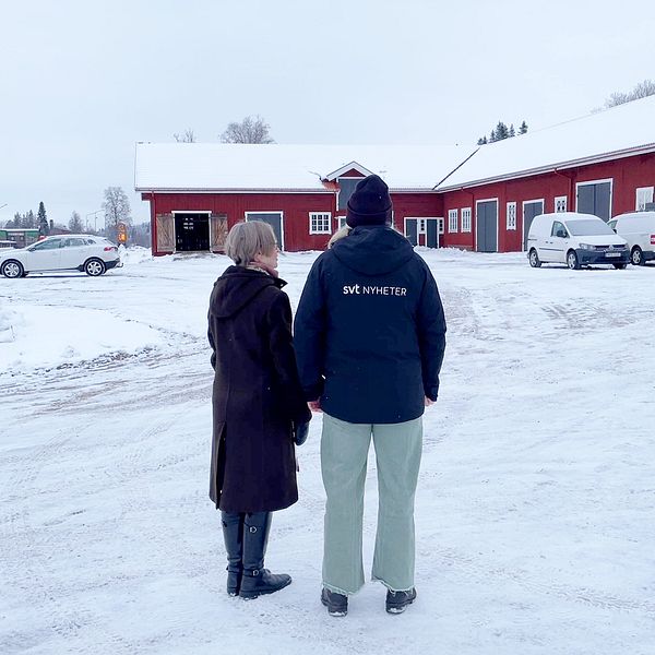 En kvinna med kort grått hår samt en kvinna med gröna byxor står framför församlingens röda, stora lada i Lima.