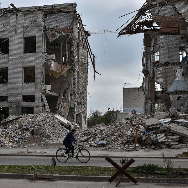 En kvinna cyklar vid en bombad byggnad i Orkihiv, Ukraina.
