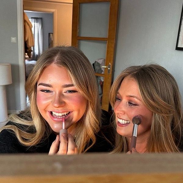 Emma Grönlund och Lovisa Skog sitter framför en spegel i ett sovrum och sminkar sig