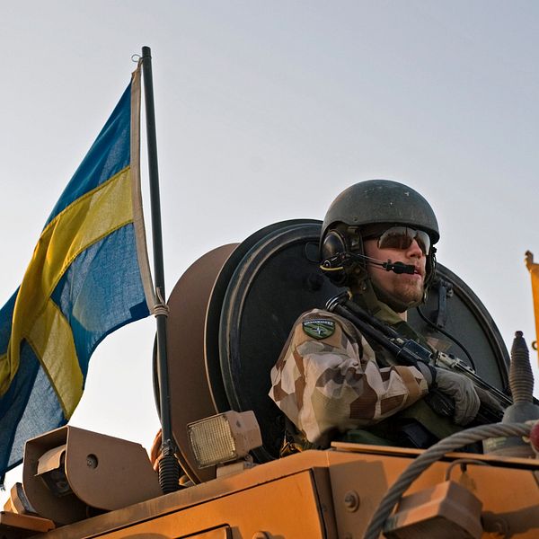 Bild på en svensk soldat med sandfärgad uniform. Svensk flaga bredvid.