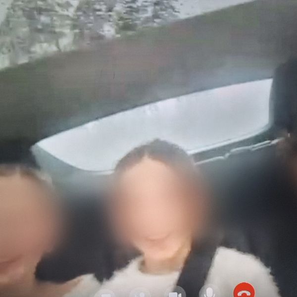 Tre personer sitter i baksätet av en bil med regniga eller dimmiga bakgrundsvyer genom bilfönstret.