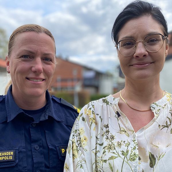 Två personer står utomhus, en i polisuniform och en i mönstrad blus. Hus syns i bakgrunden.
