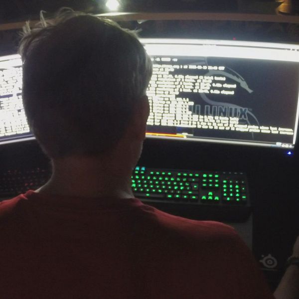 En man sitter vid en dator i mörkret och läser kod.
