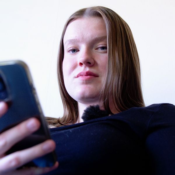 Kvinna sitter i en soffa med sin telefon.